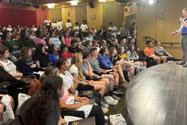 Students in a large lecture hall listen intently to a speaker on the stage.